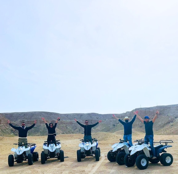 Four people on quad bikes with their arms raised in a desert landscape. 5