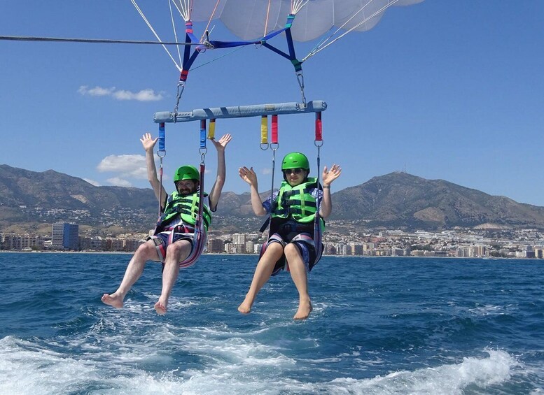 Two people parasailing over water with a cityscape and mountains in the background. 2