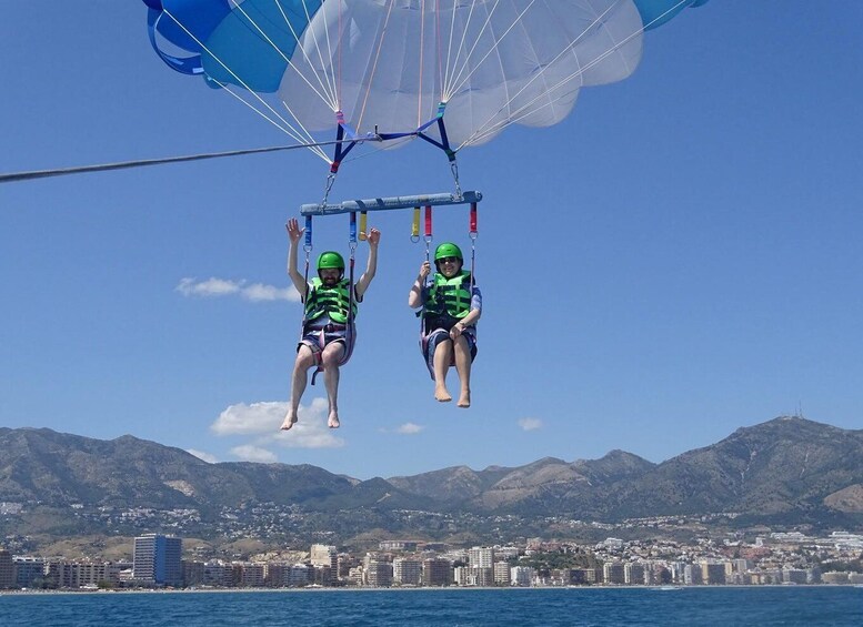 Two individuals parasailing over a coastal city with mountains in the background. 5