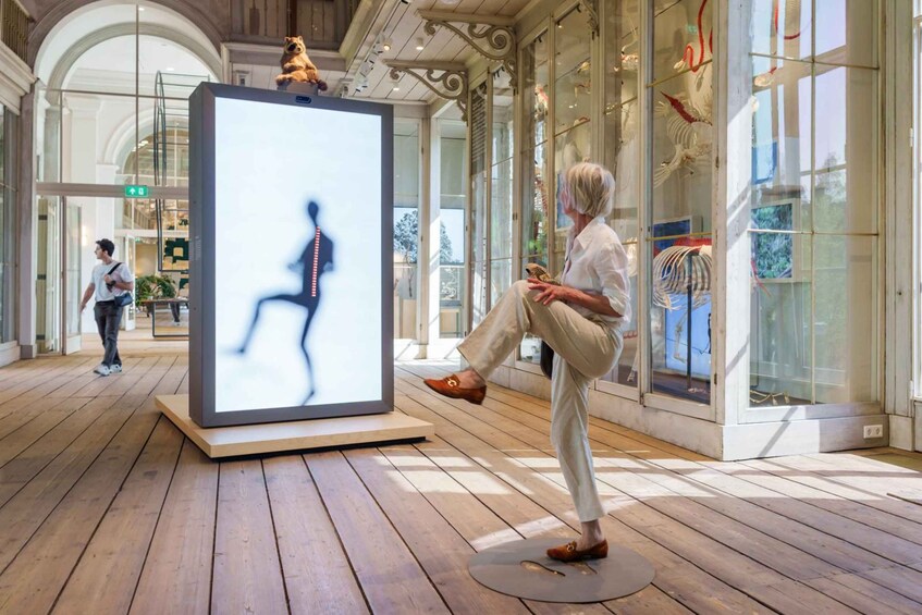A person performing a dance in a spacious, well-lit indoor area with wooden flooring and glass display cases. 5