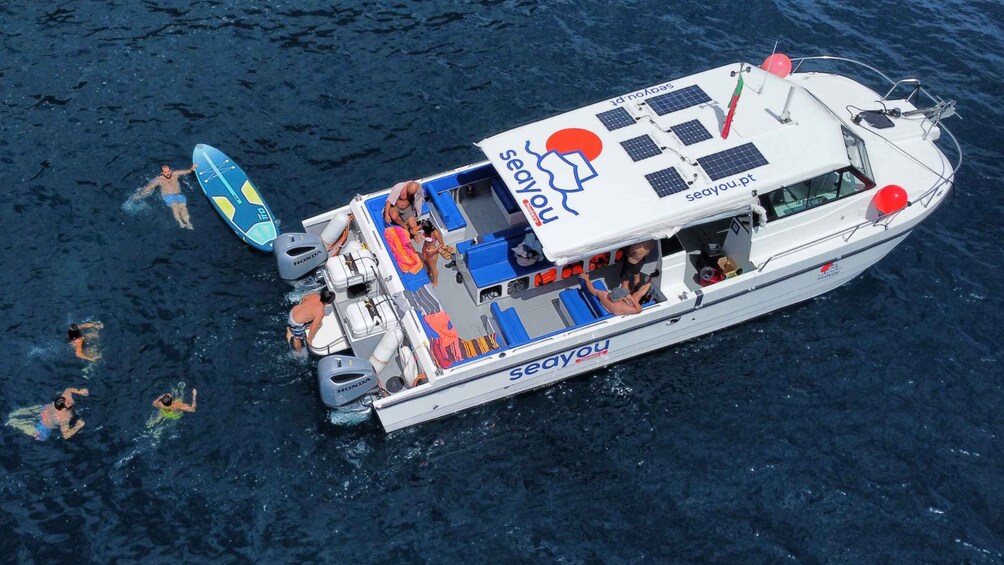 A boat with the name 'seayou.pt' and several people swimming around it. 2