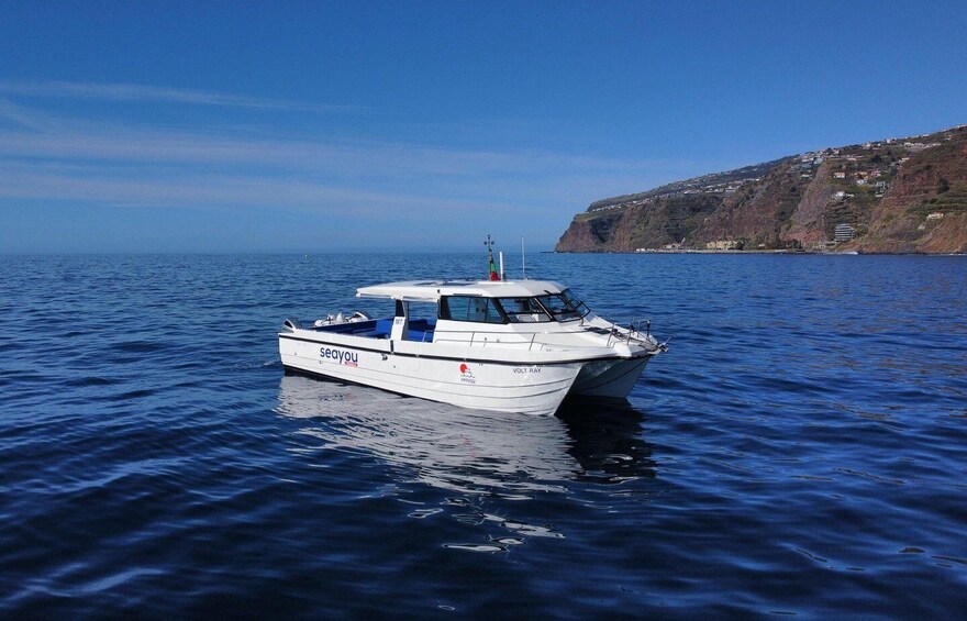 A white boat named VOLT RAY on calm blue waters with a hilly coastline in the background. 4