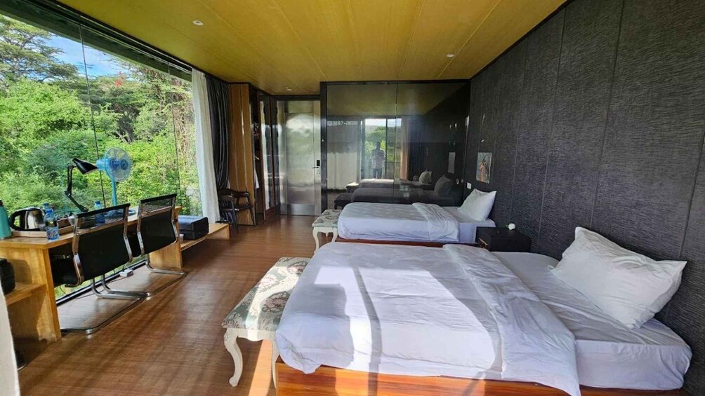 A modern bedroom with two beds, a desk, and a large window overlooking greenery. 4