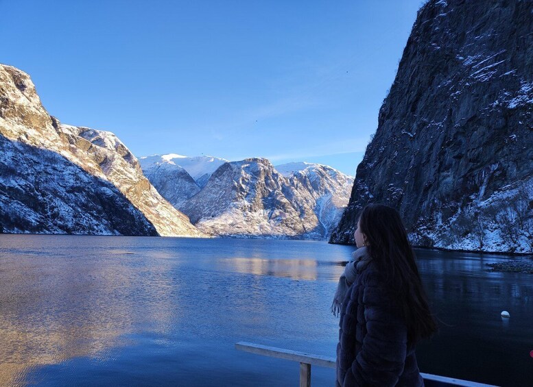 A person standing by a calm lake with snow-covered mountains in the background. 1