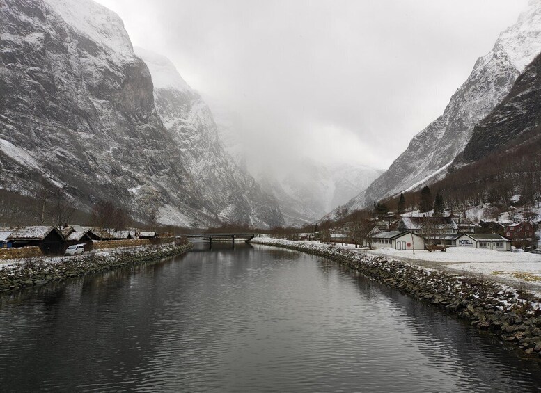 A snow-covered river with a bridge, houses, and mountains in the background. 2