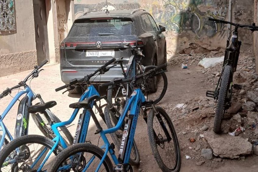 A parked car and bicycles in a rough, unpaved area with graffiti on the walls. 3