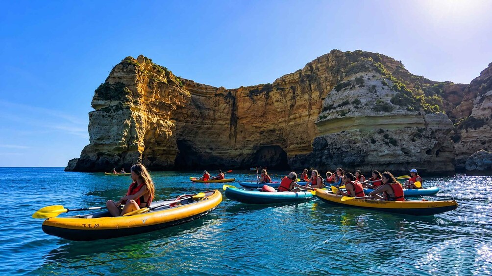 People kayaking on clear blue waters with rocky cliffs in the background. 3