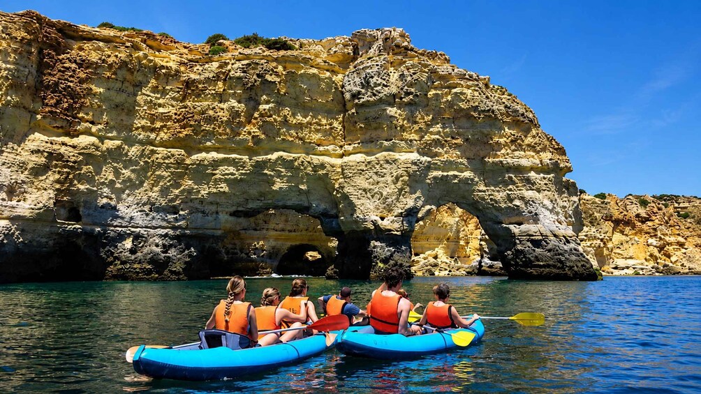 People kayaking on a calm sea with a rocky cliff in the background. 2