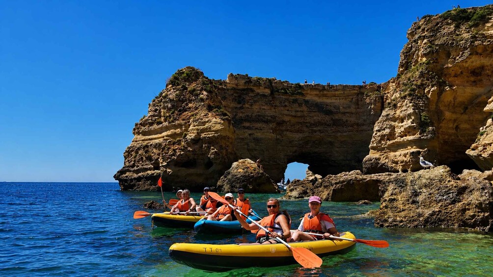 People kayaking near a rocky coastline with clear water and a large rock formation. 1