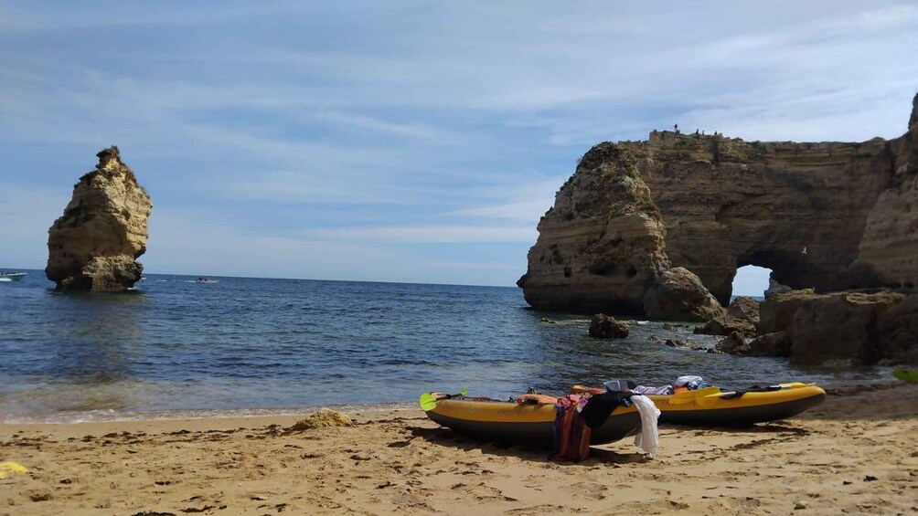A beach with kayaks and a large rock formation with an arch. 4