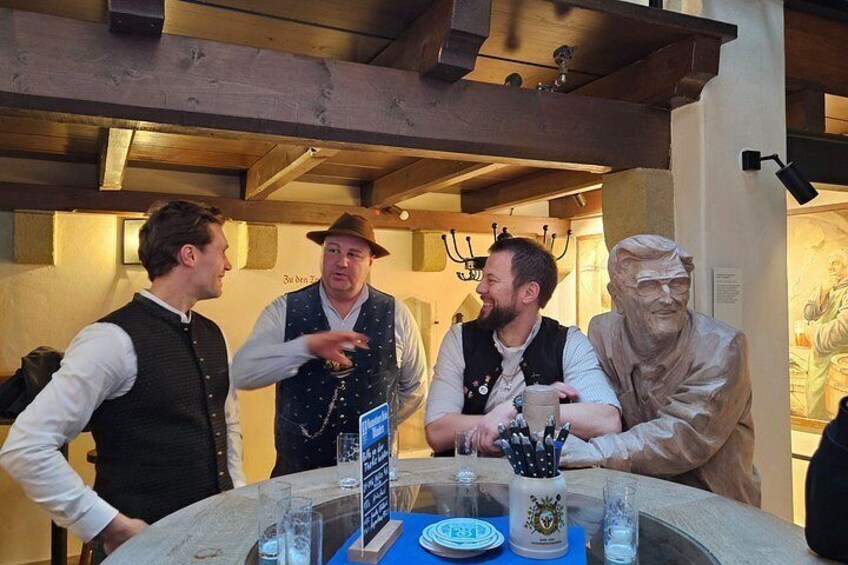 A group of people at a table with a glass of beer, a menu, and a statue in the background. 3