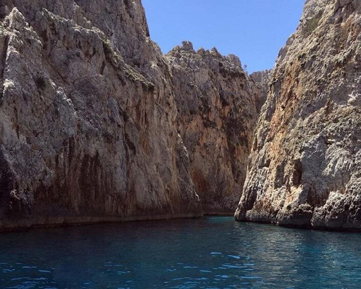 A narrow canyon with steep rocky walls and a clear blue water body at the bottom. 2