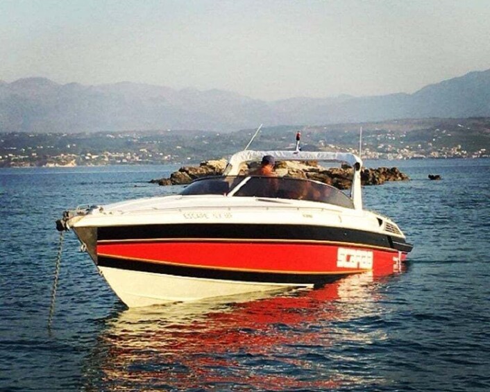 A red and white speedboat anchored in calm waters with a mountainous coastline in the background. 1