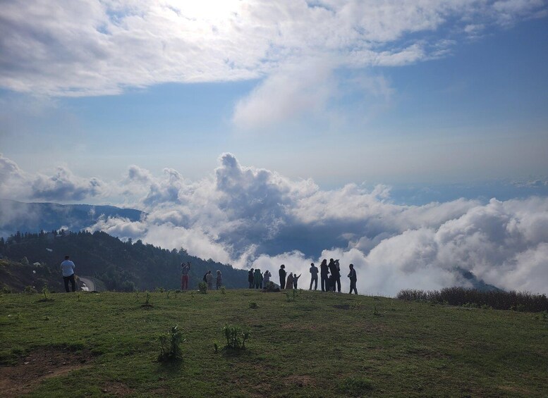A group of people standing on a grassy hill with a mountain range and clouds in the background. 5