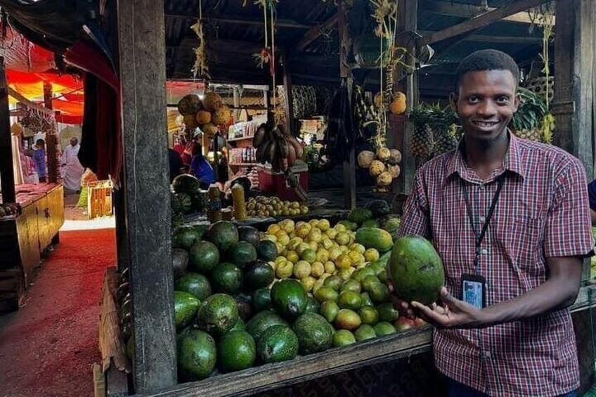 Une personne tenant un fruit vert sur un étal de marché où sont exposés divers fruits et légumes. 3