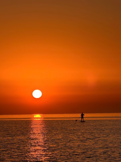 A sunset over a calm sea with a silhouette of a person paddleboarding. 2