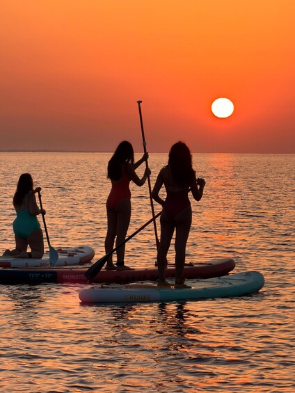 Three people paddleboarding on a calm sea during sunset. 3