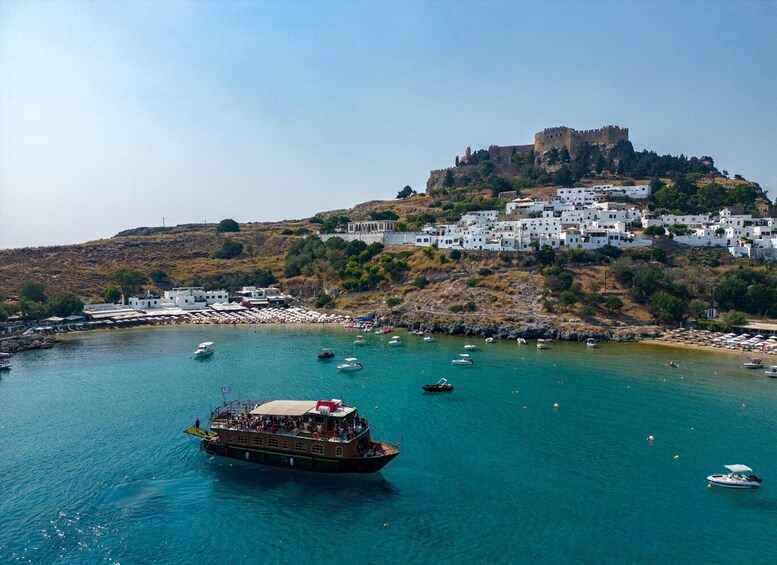 A coastal town with a castle on a hill, boats on the water, and white buildings. 1