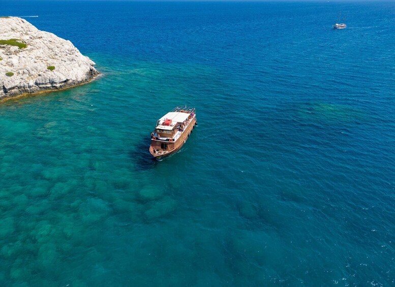 A boat in clear turquoise waters near a rocky coastline. 2