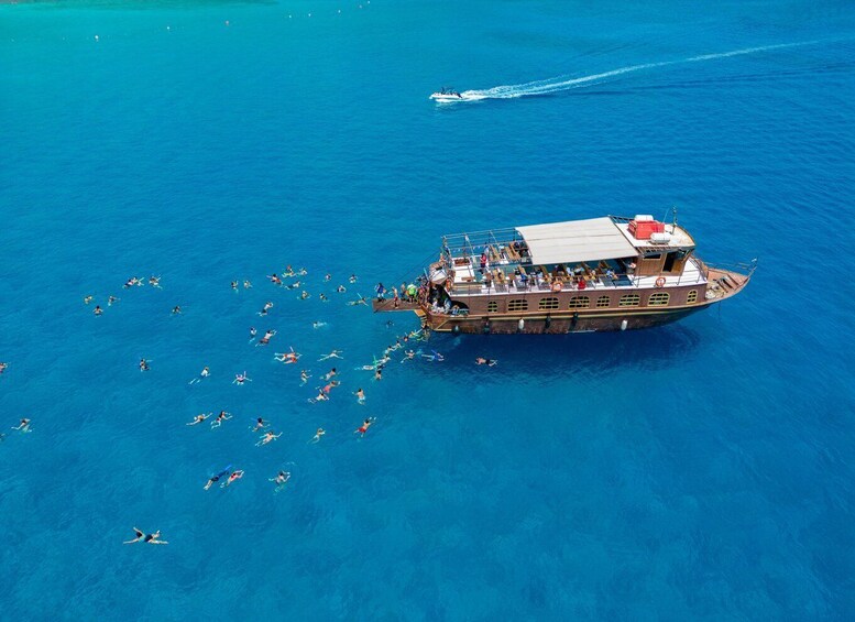 A boat with people swimming around it in a clear blue sea. 5