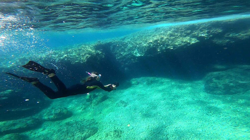 A diver underwater with a camera, surrounded by clear blue water and rocky formations. 5