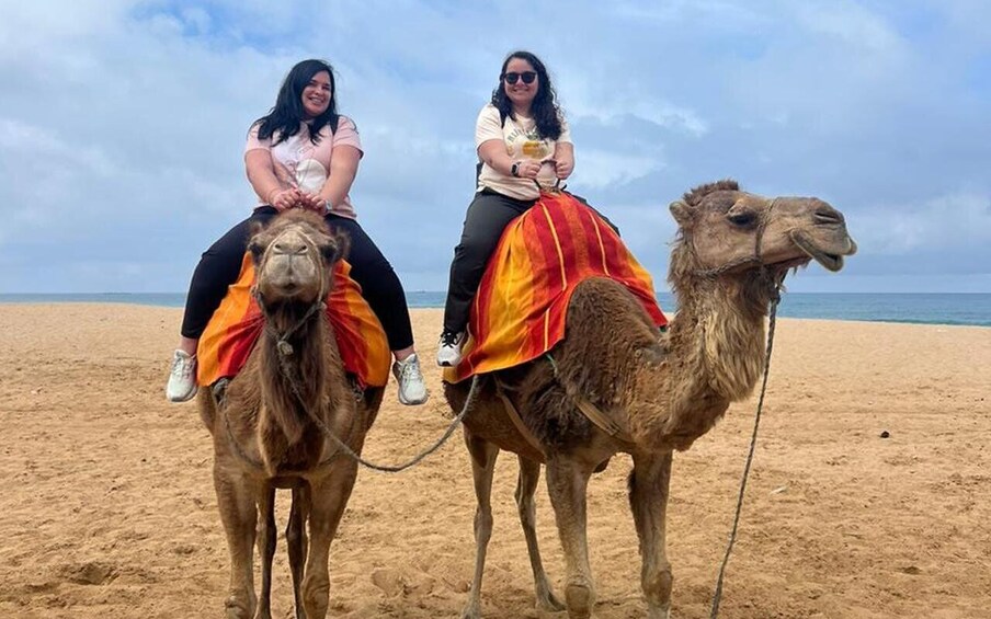 Dos personas montando camellos en una playa. 1