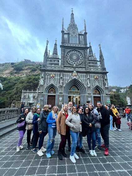 A group of people posing in front of a Gothic-style church with intricate architecture and a large circular window. 5