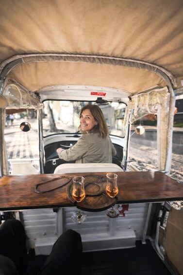 A person driving a vintage vehicle with a wooden table and two glasses of amber liquid in front. 2