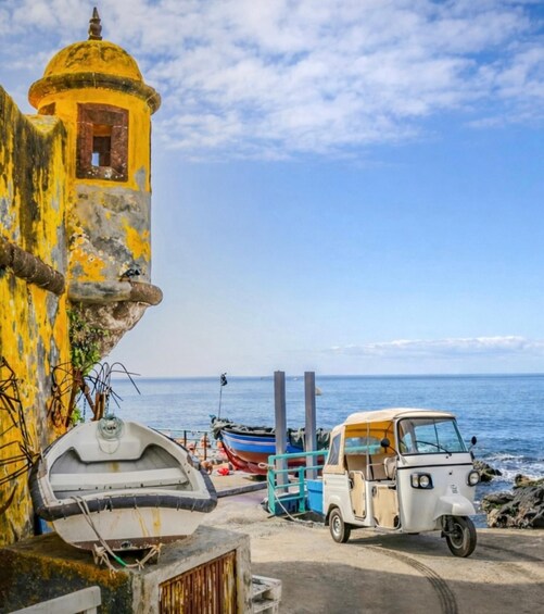 A coastal scene with a yellow building, a small boat, and a tuk-tuk parked near the water. 5