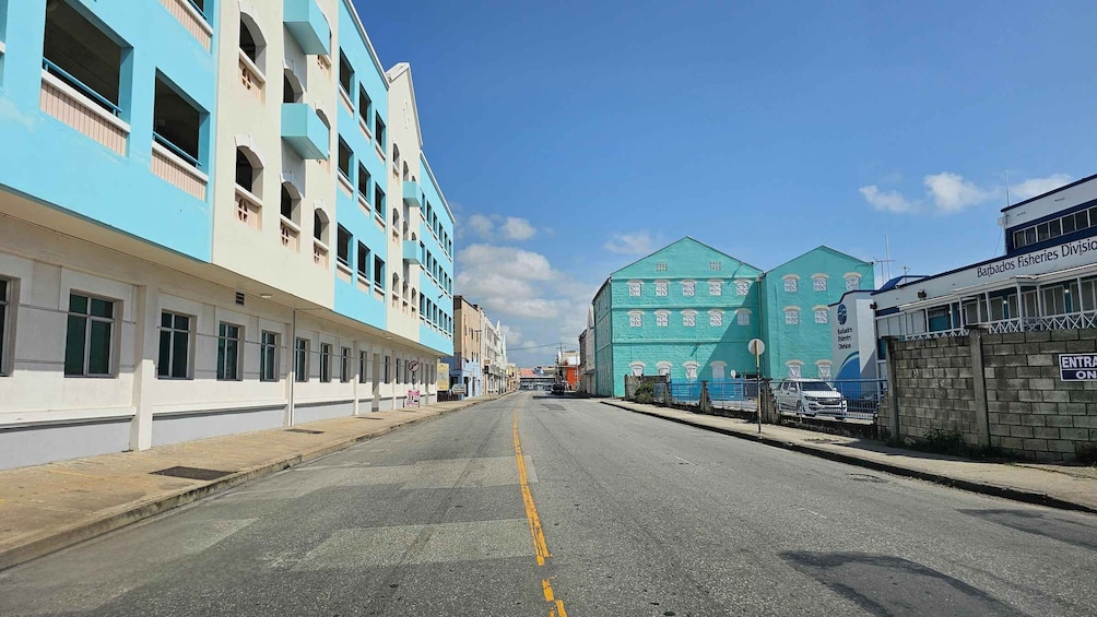 A street with buildings, including a blue and white structure and a green building with the Barbados Fisheries Division sign. 5