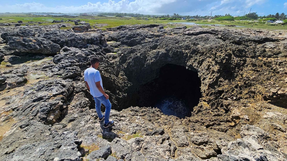 A man standing near a large volcanic crater with a small opening at the bottom. 2
