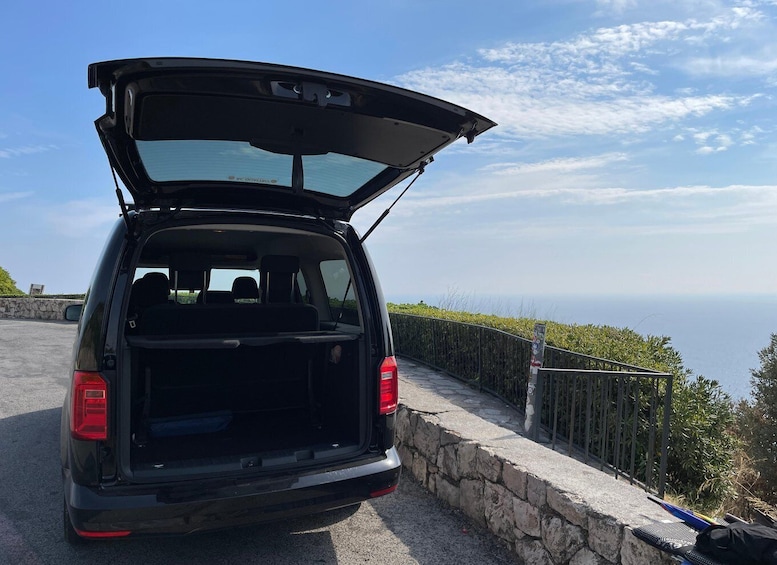 A black SUV with its trunk open, parked on a stone-paved road with a scenic view of the ocean and greenery in the background. 5
