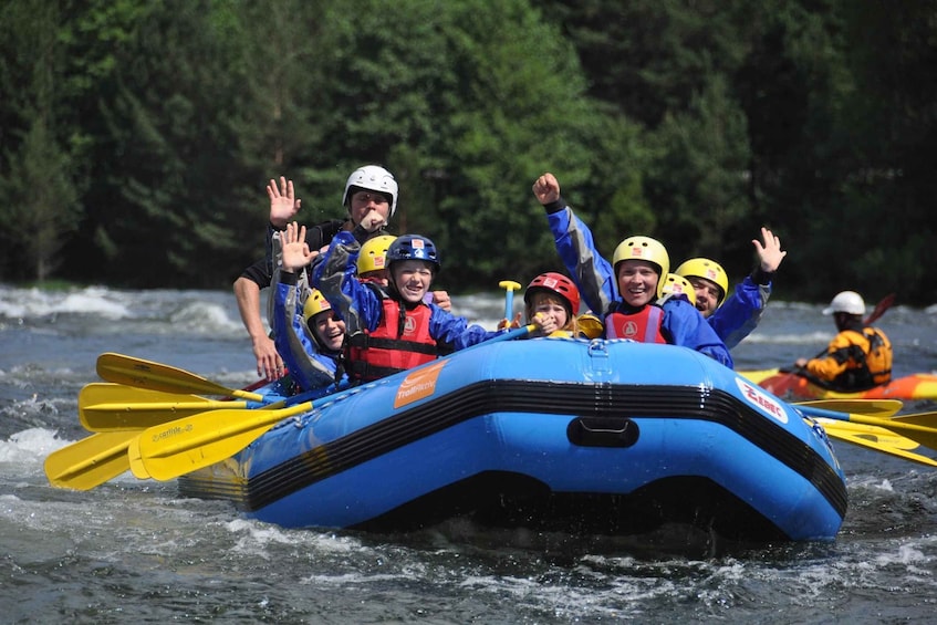 A group of people in a blue inflatable raft on a river, wearing helmets and life jackets. 1