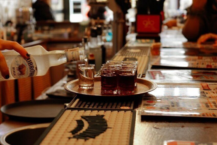 A bar setting with a person pouring a drink into a glass, a tray with multiple glasses, and a menu on the table. 5