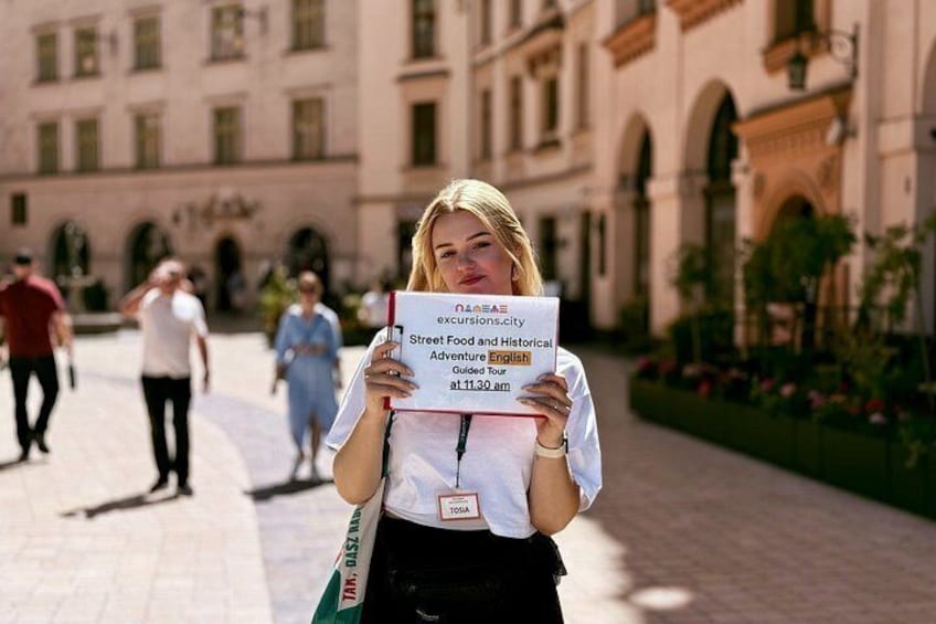 A person holding a sign in front of a building with arched windows and a paved walkway. 4