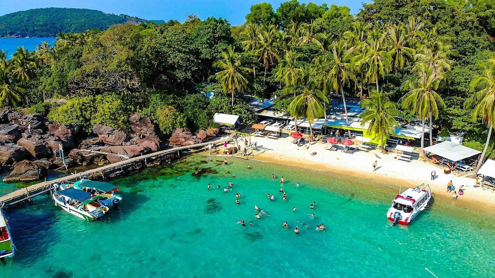 A beach with clear turquoise water, palm trees, and a pier with boats. 3