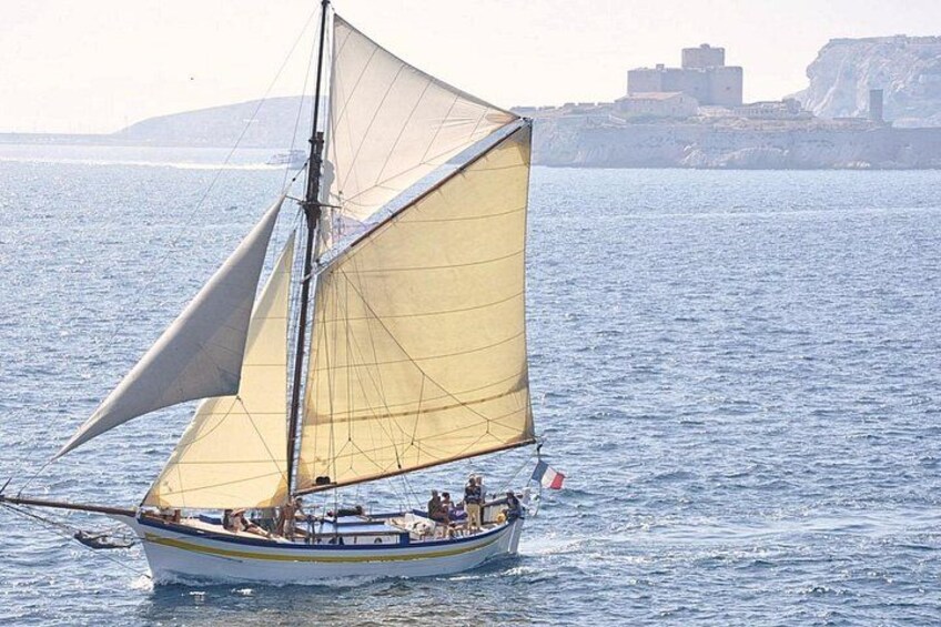 A sailboat with yellow sails on calm water, a coastline with buildings in the background, and a clear sky. 5