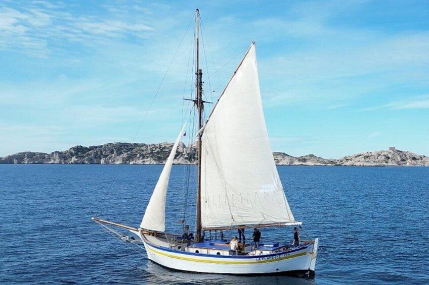 A sailboat with white sails on calm blue water, a rocky shoreline in the background, and a clear sky. 2