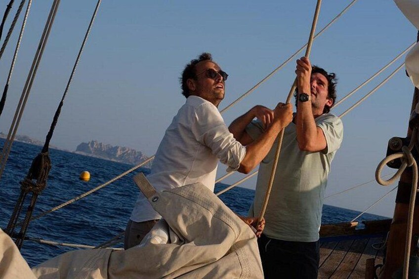 Two people on a sailboat with ropes and a body of water in the background. 3