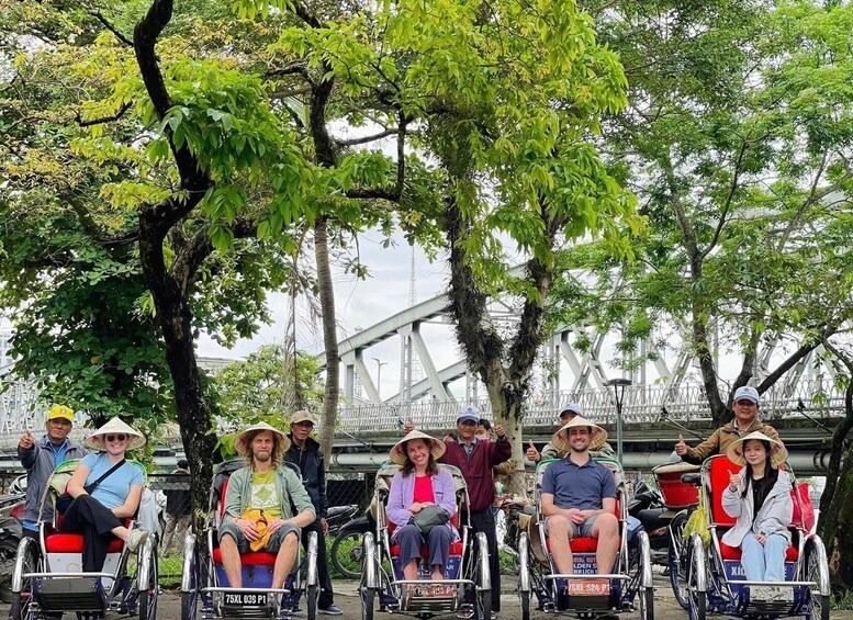 A group of people in wheelchairs near a bridge with trees in the background. 3