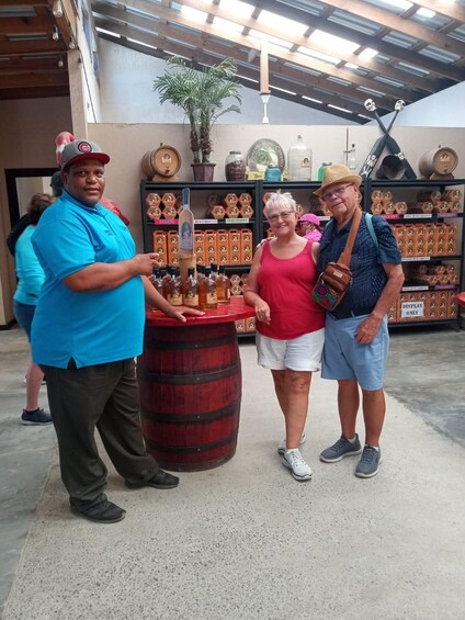 Three people standing in a store with shelves of bottled beverages and a large barrel. 4