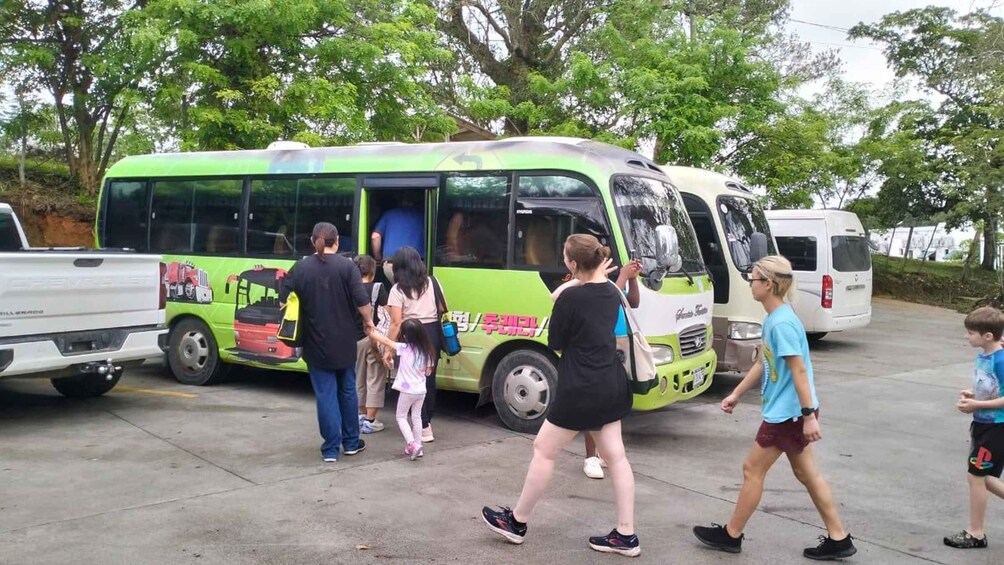 A green bus with passengers boarding, parked in a lot with trees and other vehicles. 3