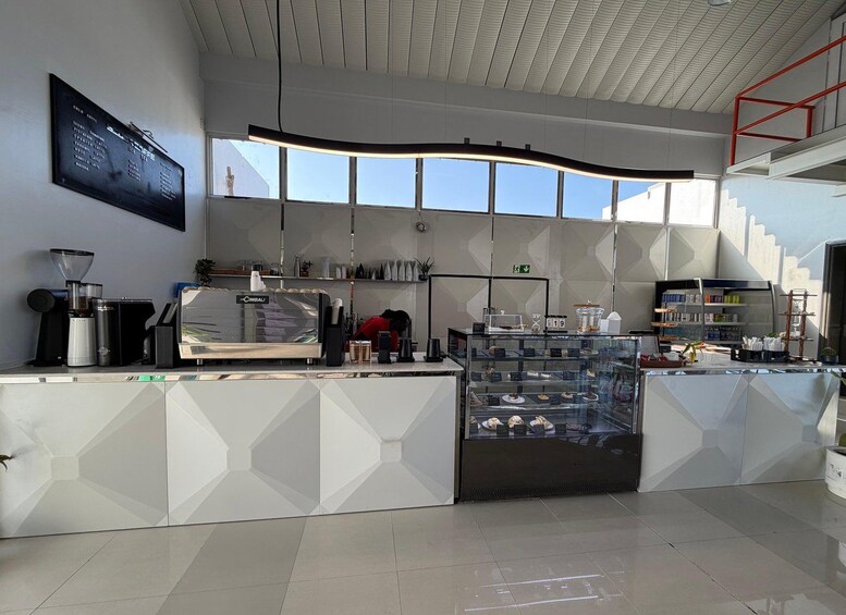A modern cafe interior with a coffee machine, a glass display case with pastries, and a menu board. 4