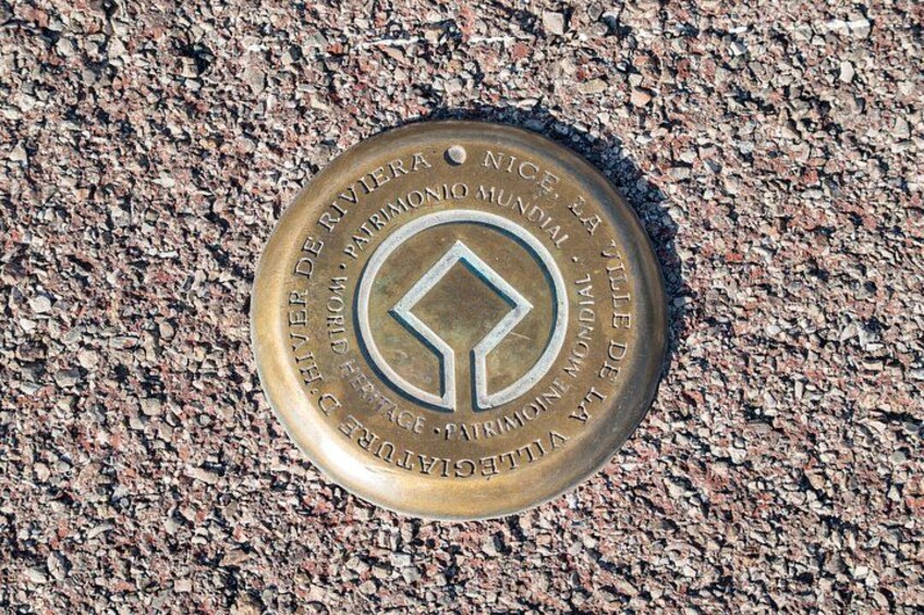 Eine Metallplatte mit Inschriften und einem diamantförmigen Emblem auf einer strukturierten Oberfläche. 2