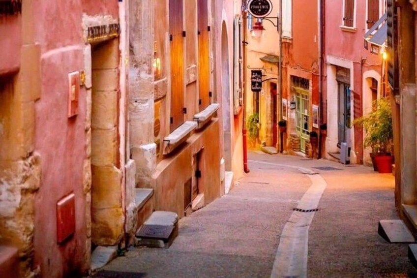 Une rue étroite, bordée de bâtiments des deux côtés, une enseigne suspendue à un bâtiment et un pot de fleurs sur la droite. 3