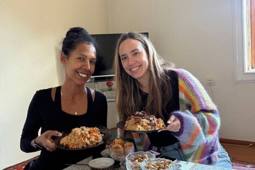 Deux personnes sont assises à une table, chacune tenant une assiette de nourriture, avec un téléviseur en arrière-plan. 3