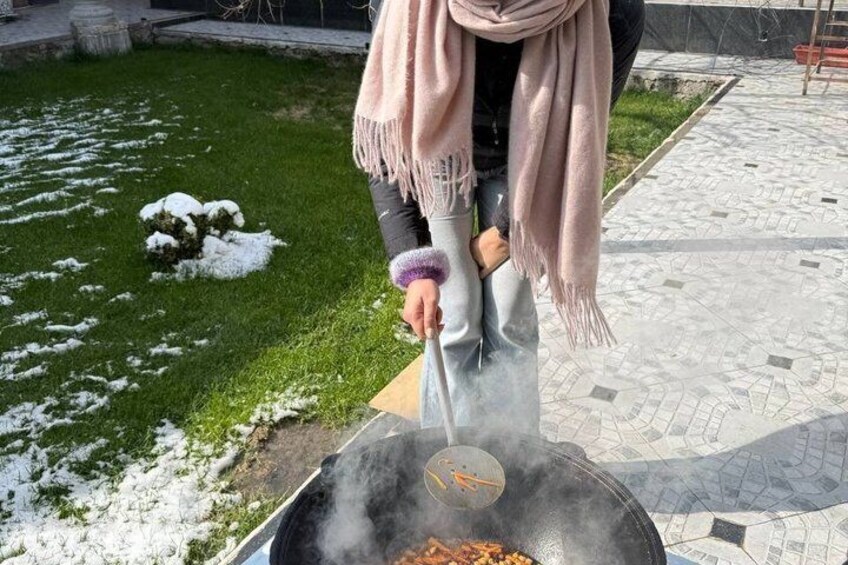 Une personne cuisine à l’extérieur, sur un réchaud, avec une poêle. De la neige recouvre le sol, et un chemin pavé est visible. 5