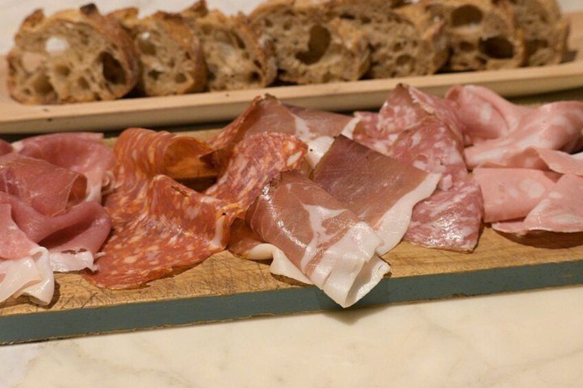 Sliced cured meats on a wooden board, with a loaf of bread in the background. 5