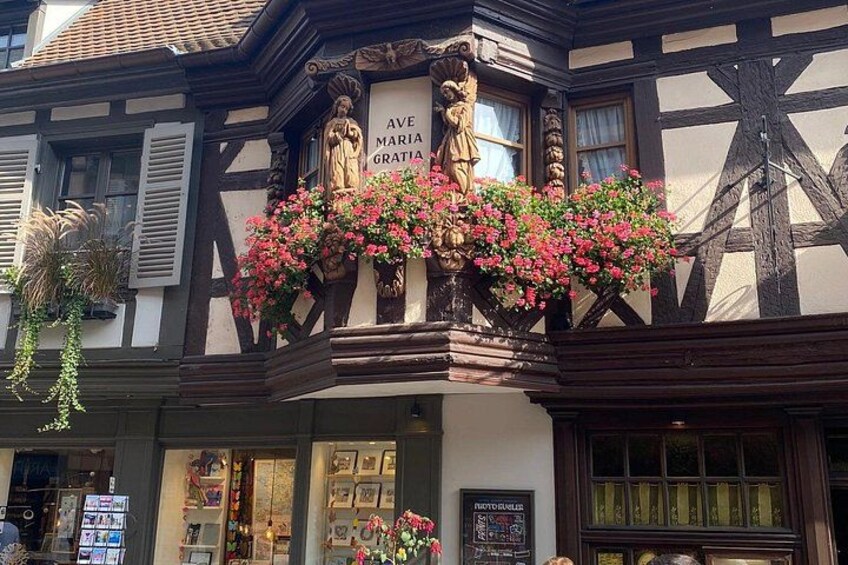 A building with a balcony adorned with pink flowers and a statue of a woman. 3