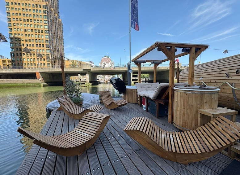 A wooden deck with lounge chairs, a hot tub, and a pergola, overlooking a river with a bridge and buildings in the background. 3